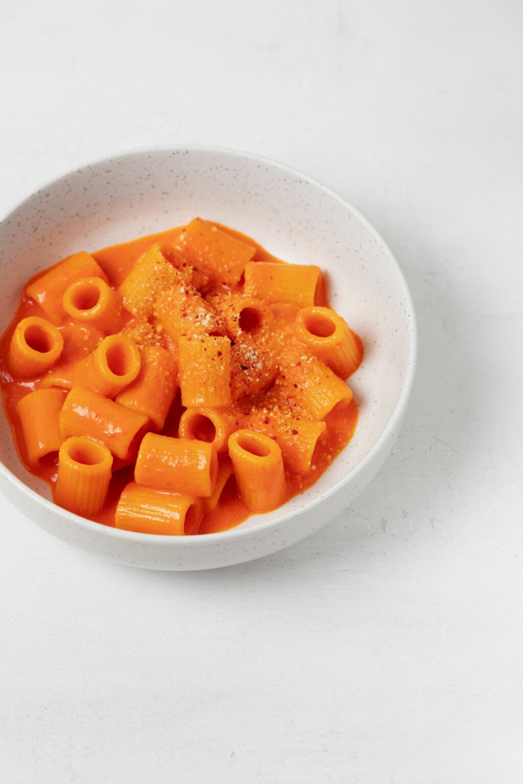 A bowl of creamy red pepper pasta has been topped with a vegan 