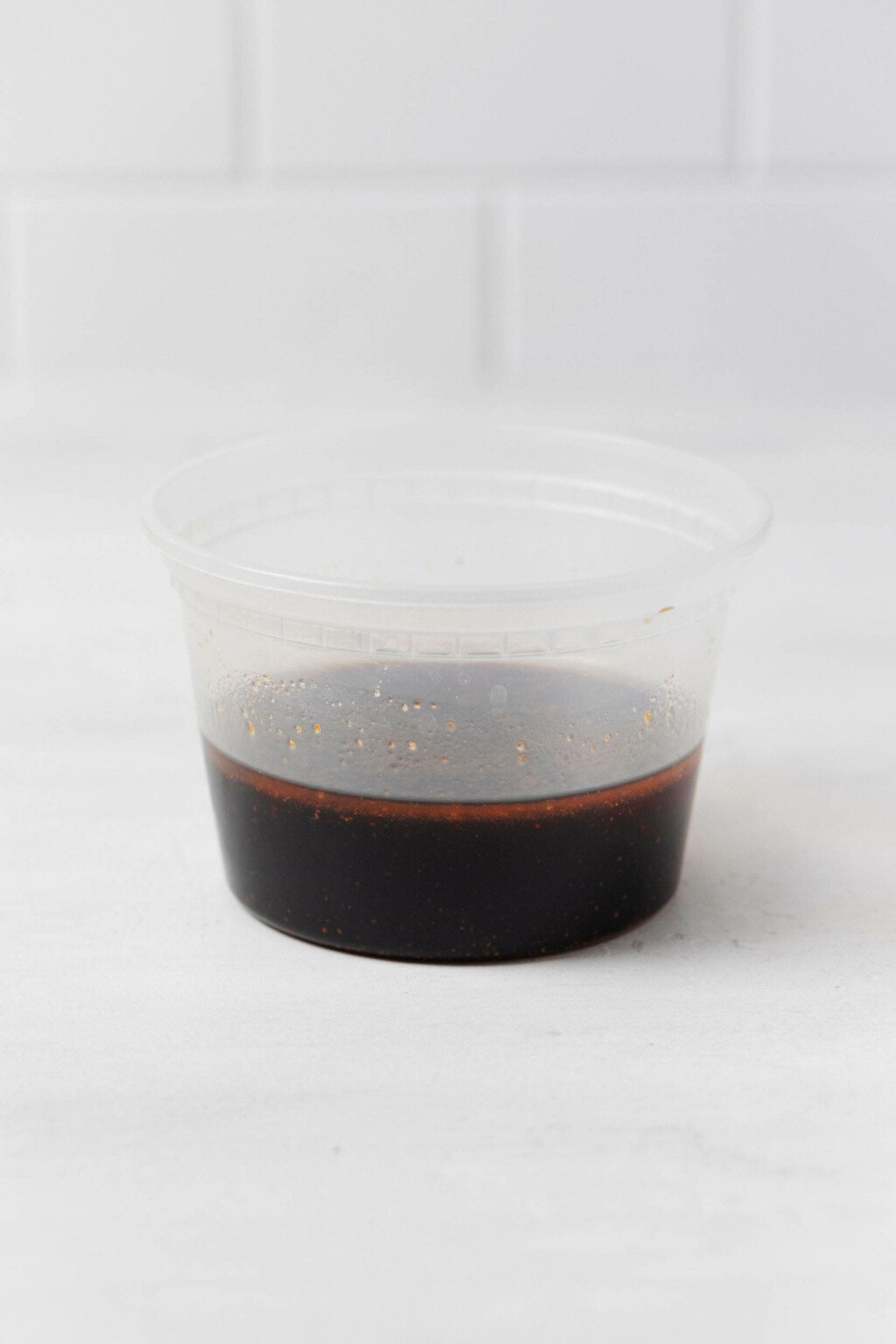 A clear, round plastic container holds a brown marinade.