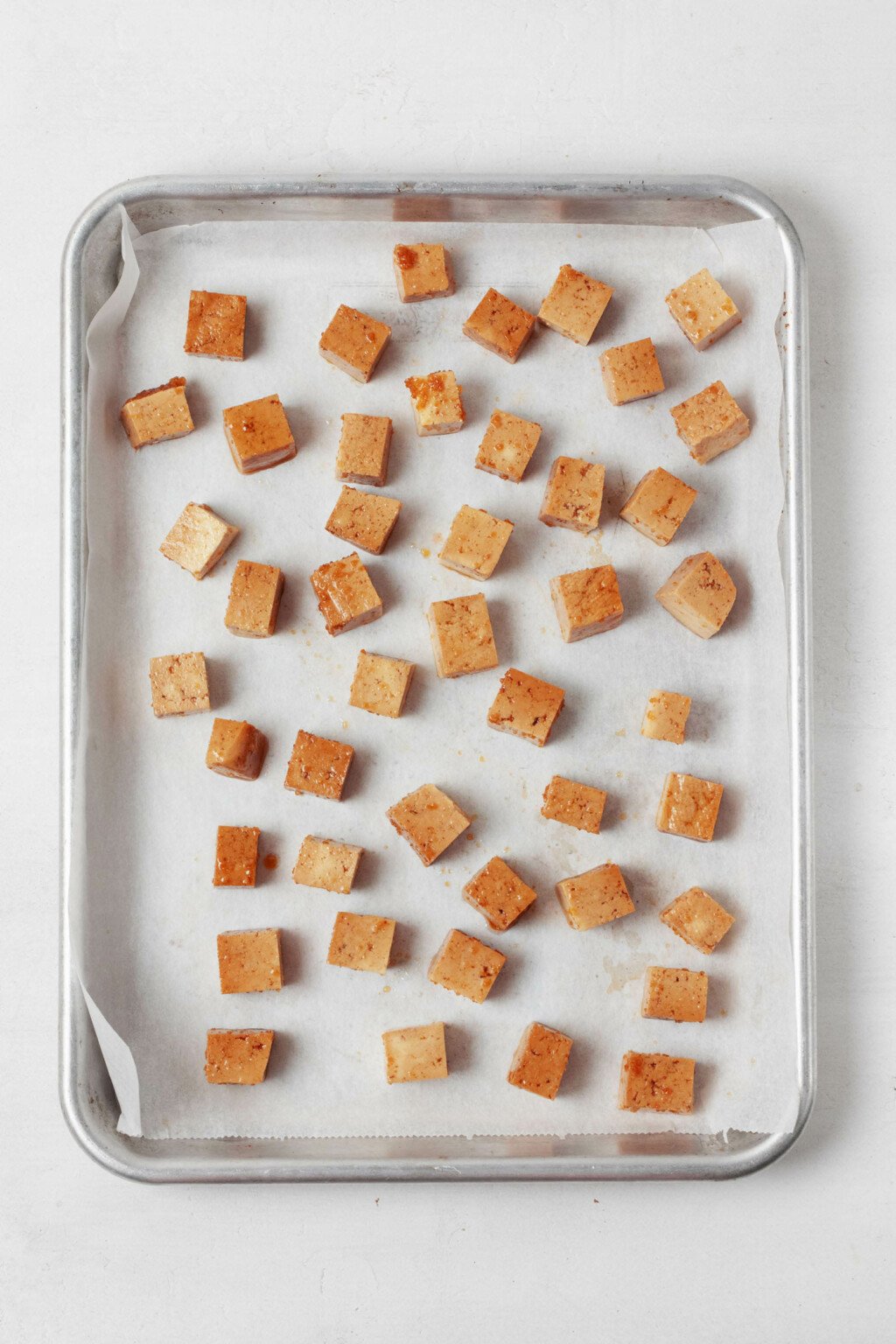 A parchment lined baking sheet holds cubes of tofu.