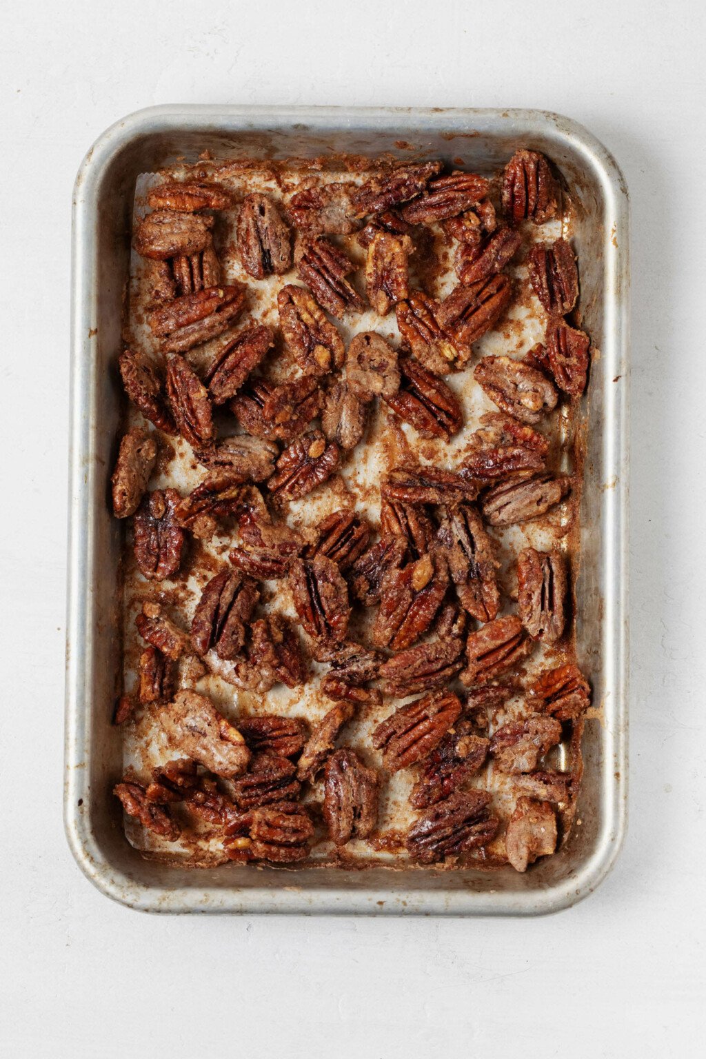 Crispy, baked pecan halves are resting on a baking sheet, fresh out of the oven.