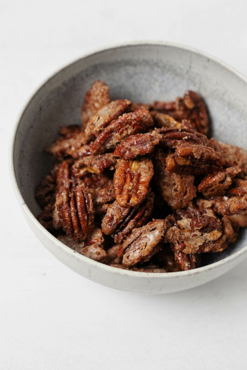 A gray, ceramic bowl is filled with crispy vegan candied pecans.