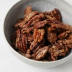 A gray, ceramic bowl is filled with crispy vegan candied pecans.