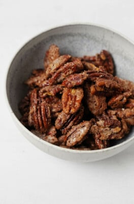 A gray, ceramic bowl is filled with crispy vegan candied pecans.