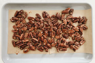 Pecan halves have been coated with sugar and spice and placed on a parchment lined baking sheet, for baking.