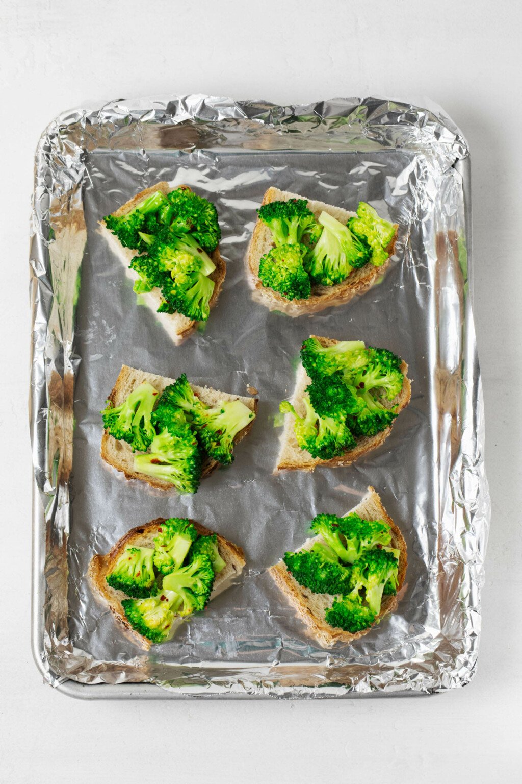 Slices of halved bread are topped with bright green, cooked broccoli florets.