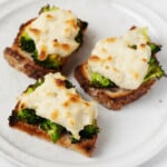 Three half-slices of vegan broccoli melts are laid out on a white, rimmed plate. The plate rests on a white surface.