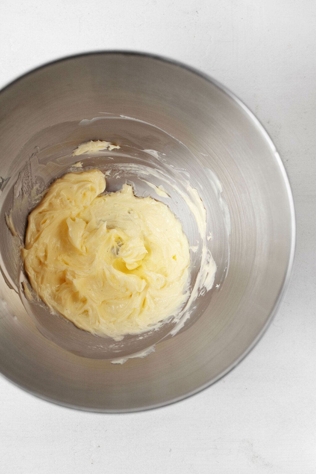 Beaten butter is resting in the silver bowl of a stand mixer.