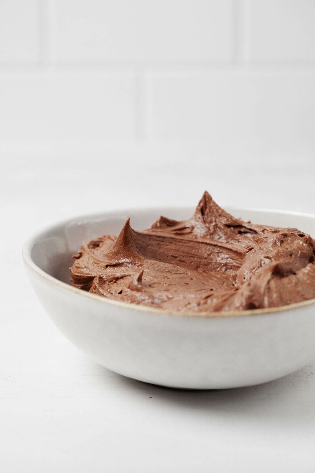 A round, ceramic, pale white gray bowl has been used to hold a rich buttercream icing.