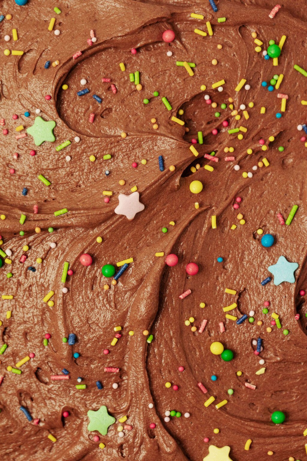 A close-up image of swirls of chocolate buttercream and sprinkles, which have been used to frost a cake.