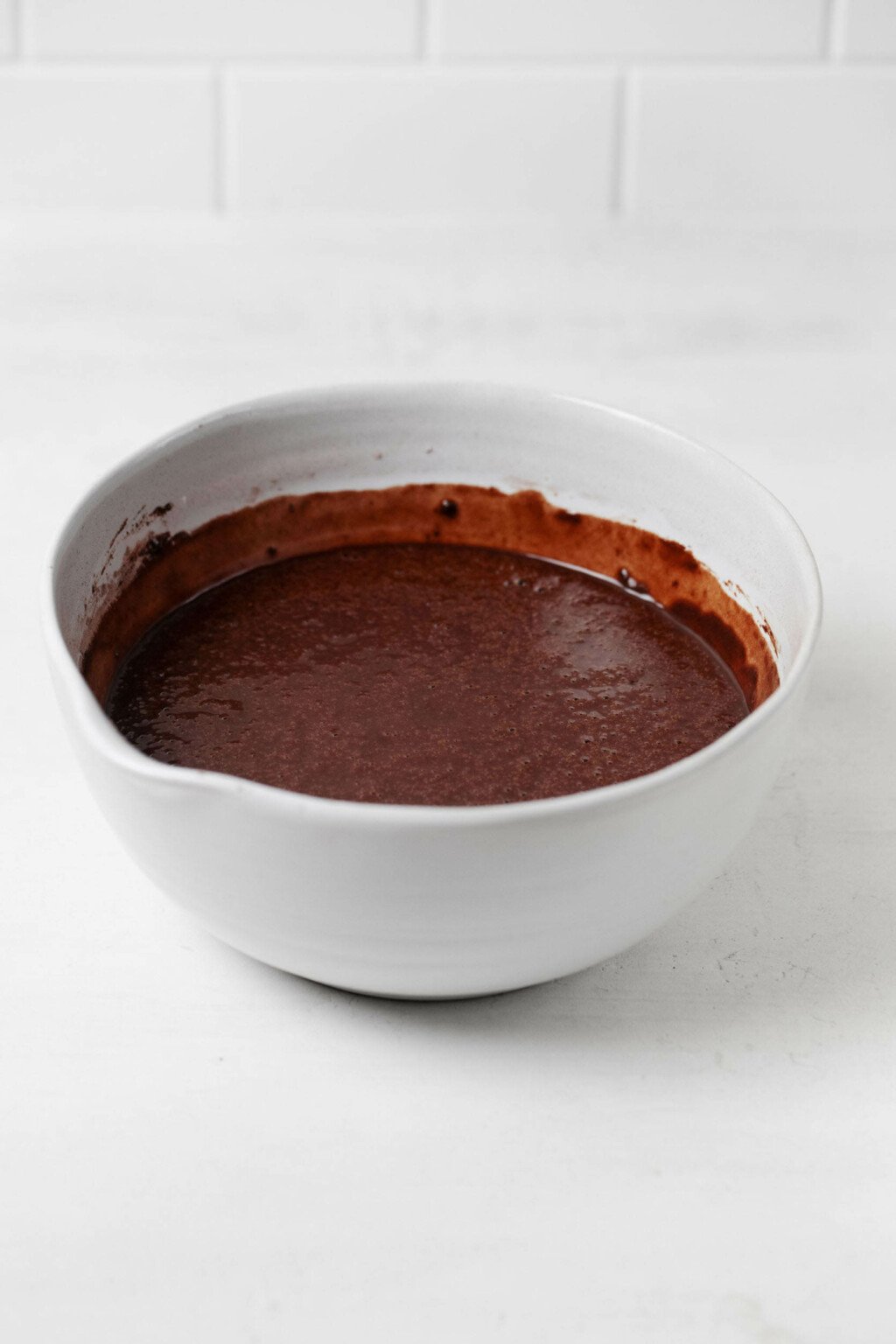 A large, white mixing bowl is filled with a chocolate cake batter.