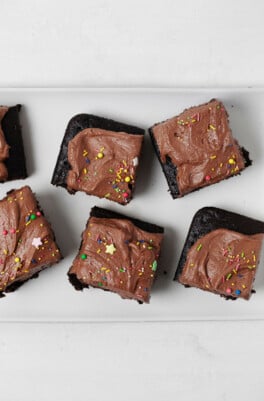 Frosted squares of a snack cake are laid out on a white platter. Each square is topped with decorative sprinkles.