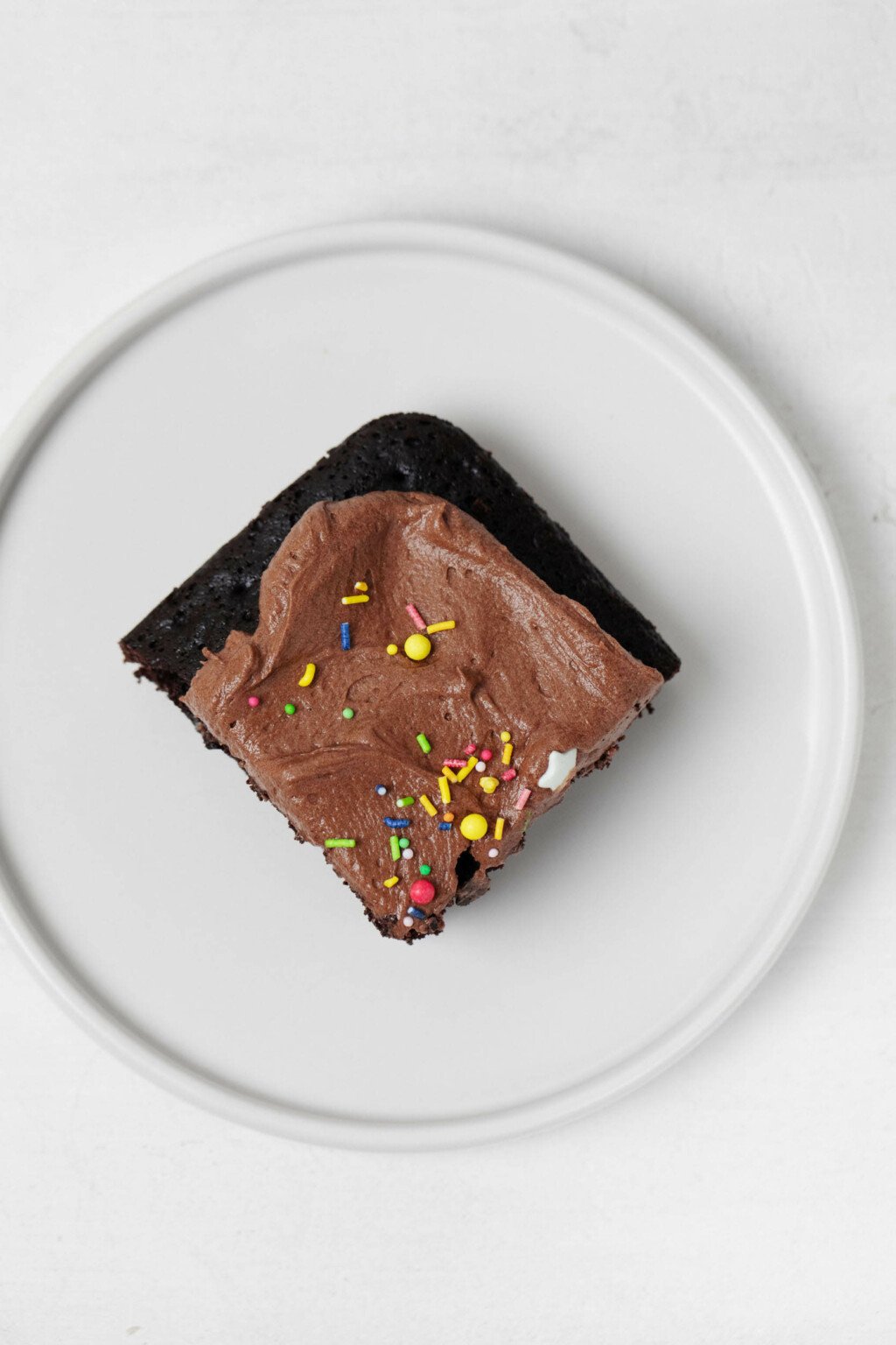 A square slice of chocolate snack cake served on a round, white plate.