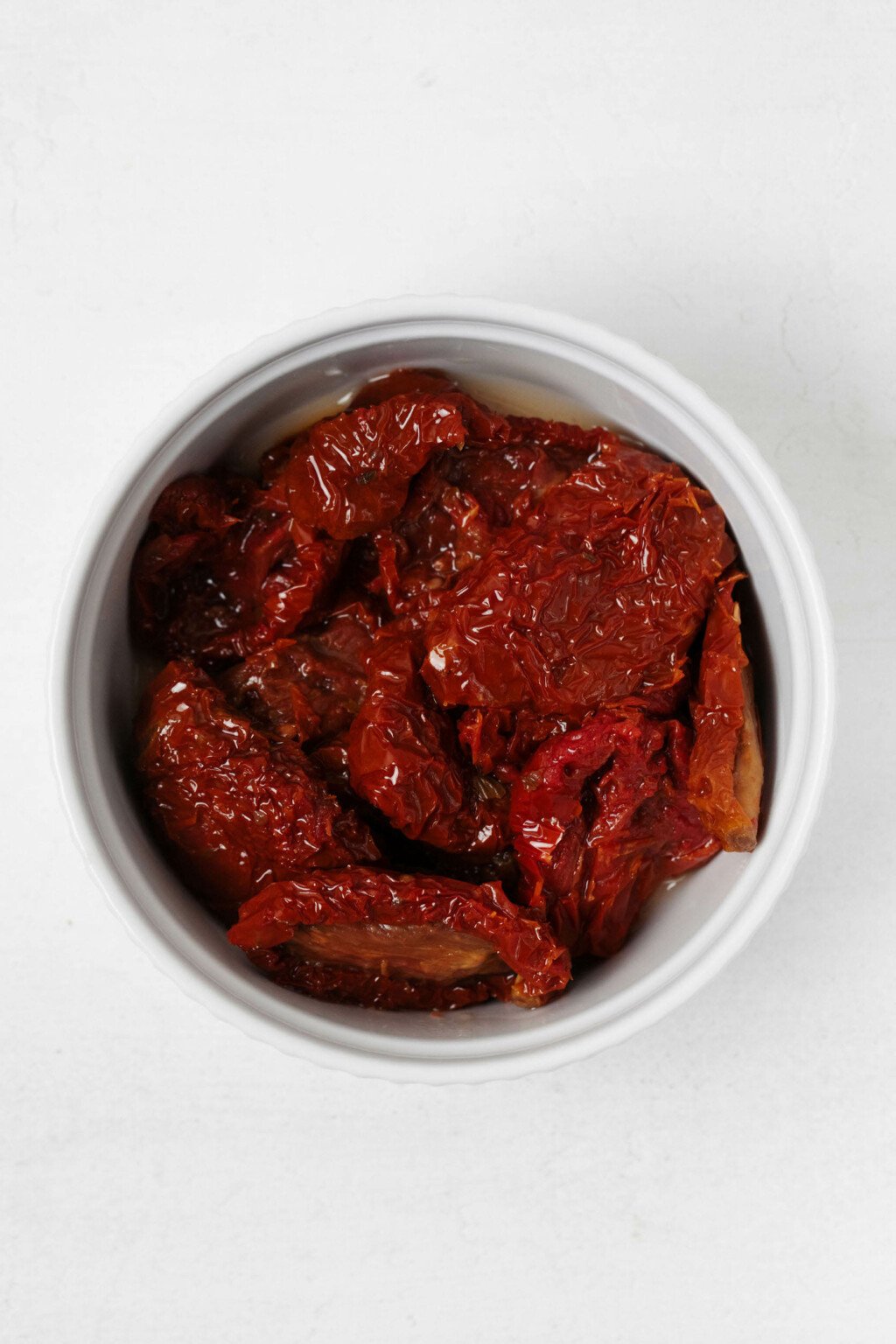 Sun-dried tomato halves have been placed into a small, round white bowl.