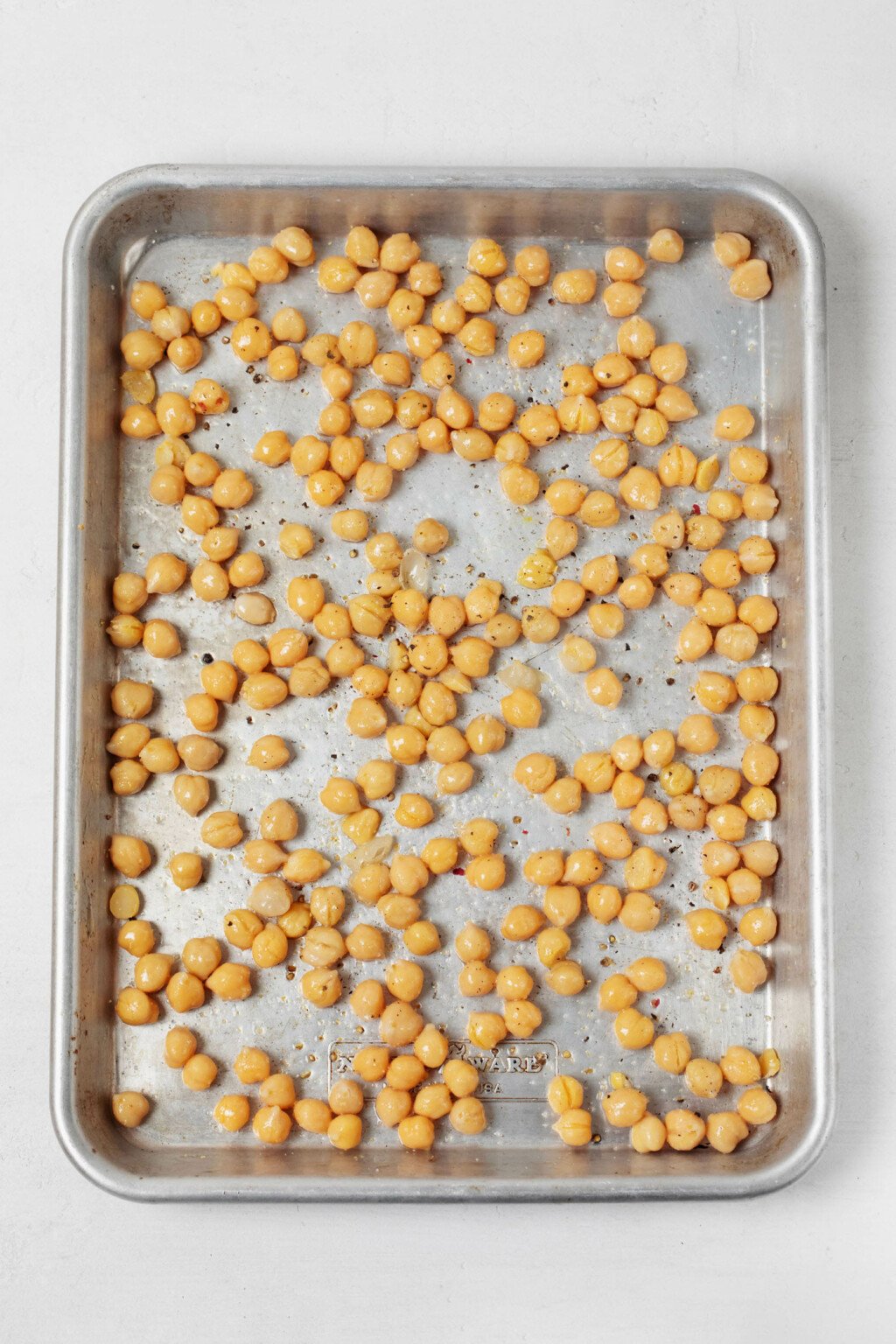 Chickpeas, which have been seasoned with oil, salt, and pepper, are on a metal baking sheet.