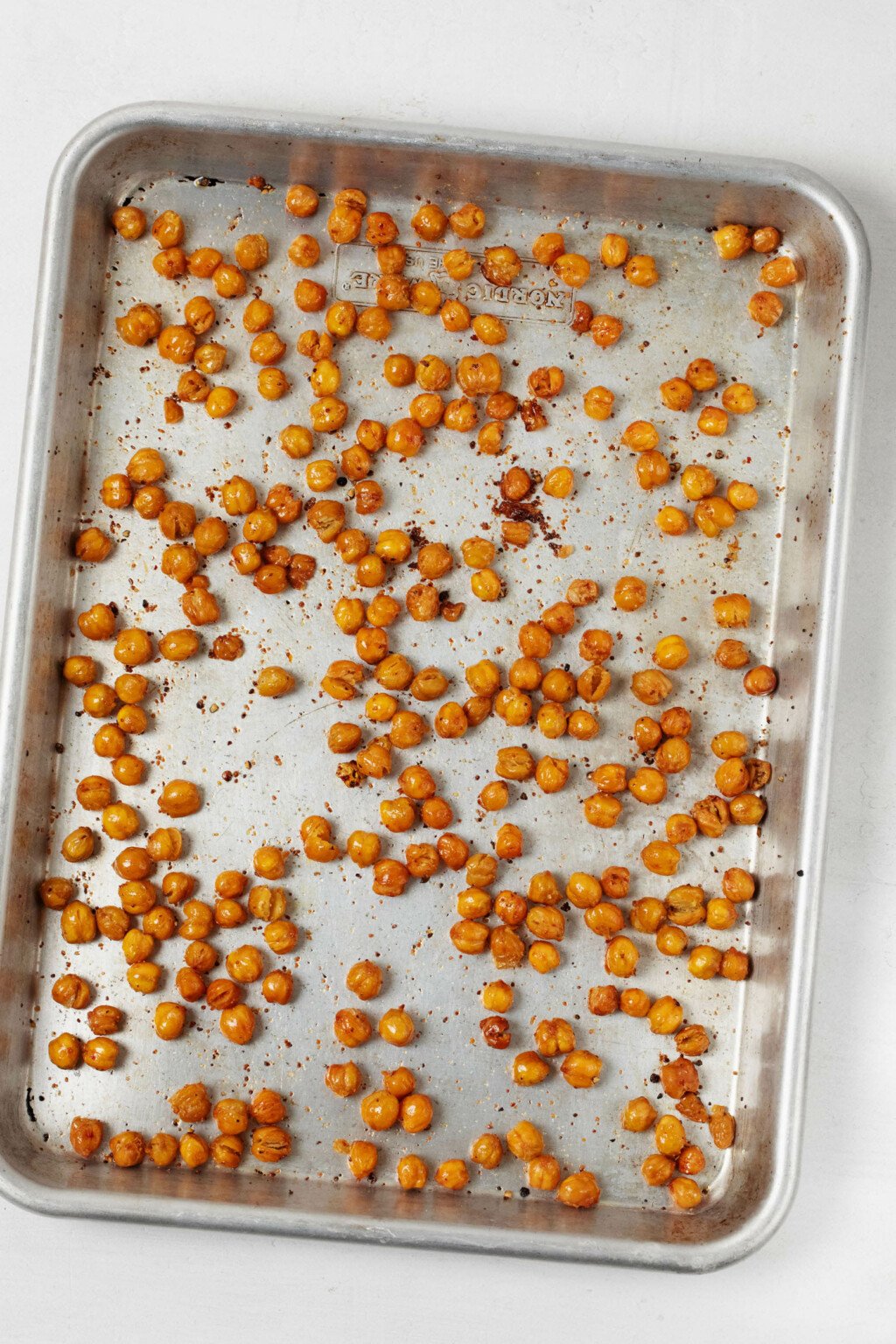An aluminum baking sheet is covered in crispy roasted chickpeas, which have just been pulled from the oven.