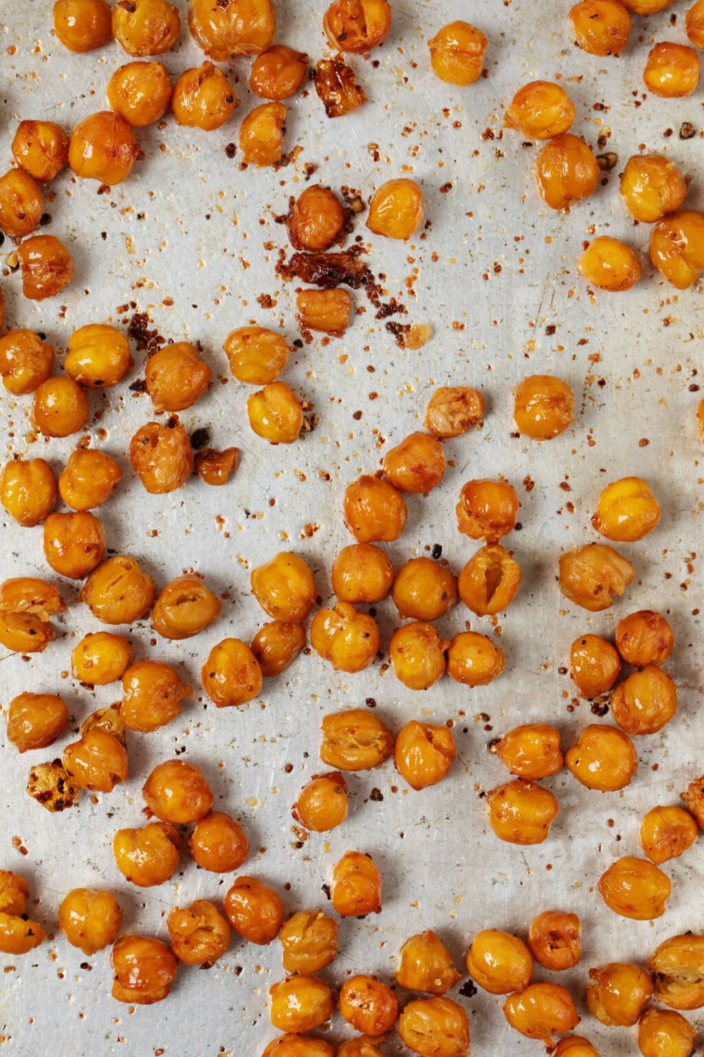 An overhead, close-up image of crispy roasted chickpeas, which are laid out with their crumbs on a metal baking sheet.