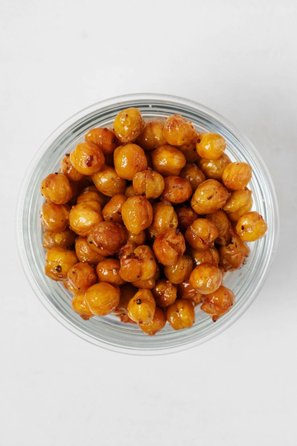 A round, glass mason jar holds crispy roasted chickpeas. It rests on a white surface.