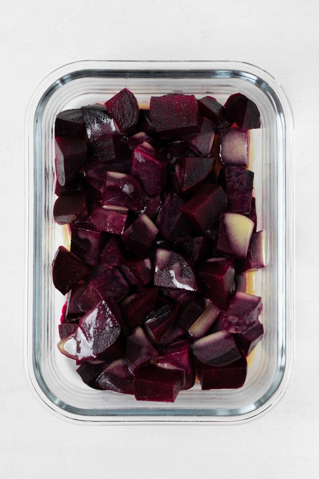 Roasted root vegetables are packed into a clear, glass-lock container. There's a bright colored vinaigrette on top.