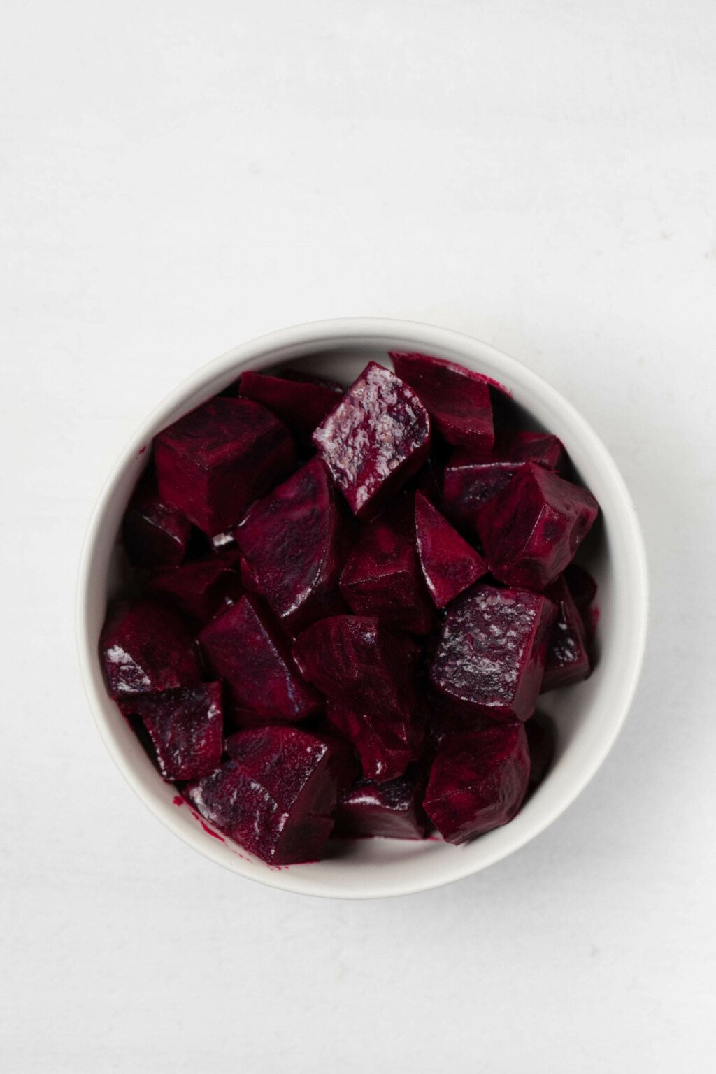 An overhead image of a small white bowl, which is filled with marinated beets.