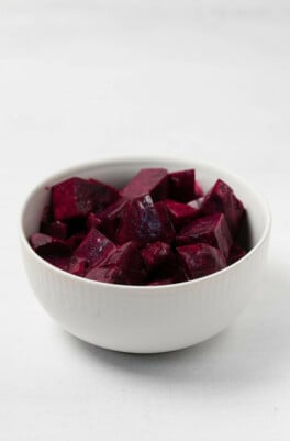 A small, round white bowl has been filled with marinated beets.
