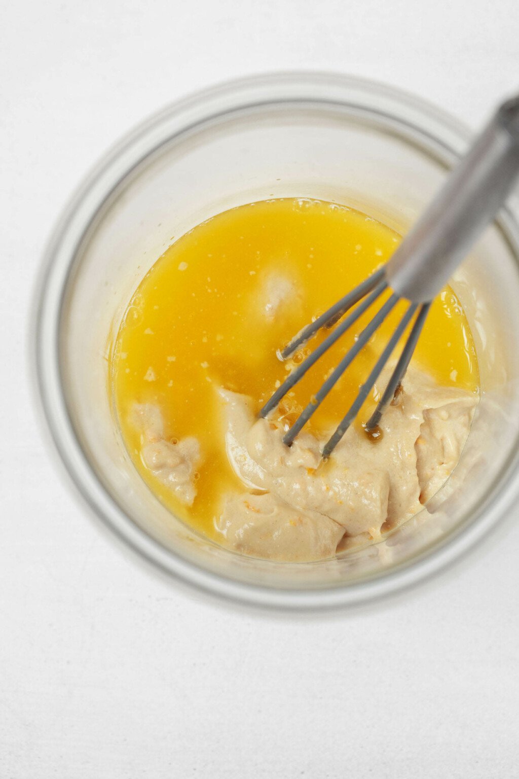 Freshly squeezed orange juice and thick, creamy tahini are being mixed with a small metal whisk.