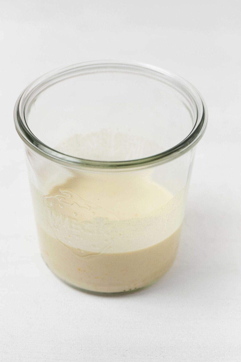 An overhead image of a creamy, off-white orange tahini dressing, which has been poured into a glass mason jar.