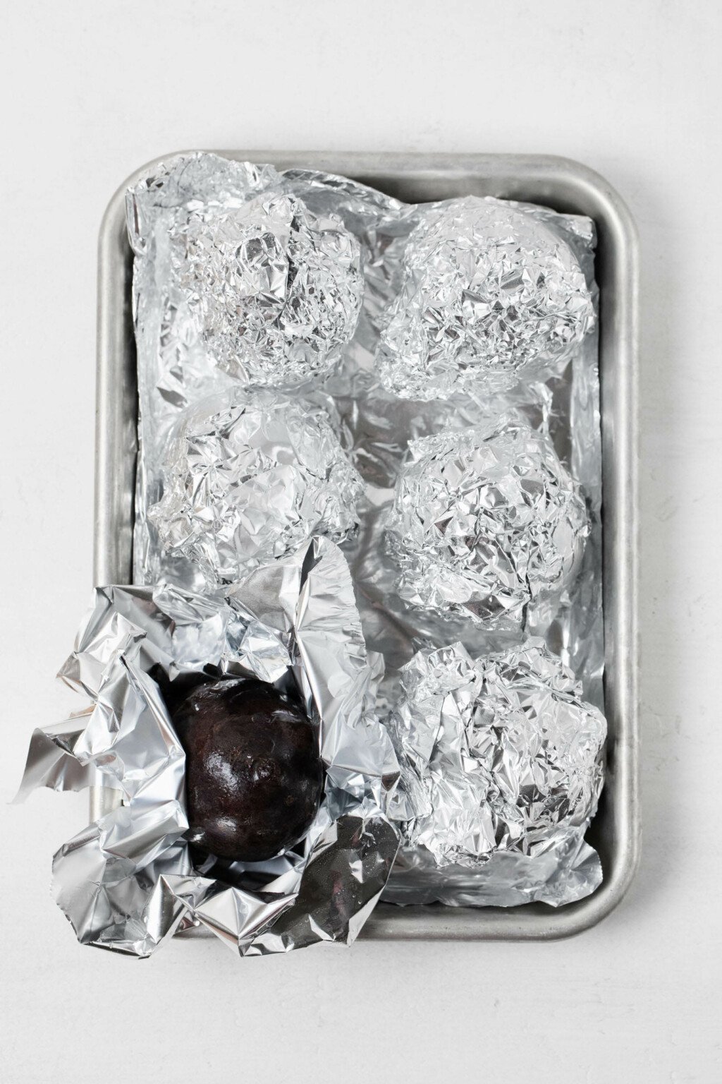 A small, aluminum baking tray contains foil-wrapped vegetables.