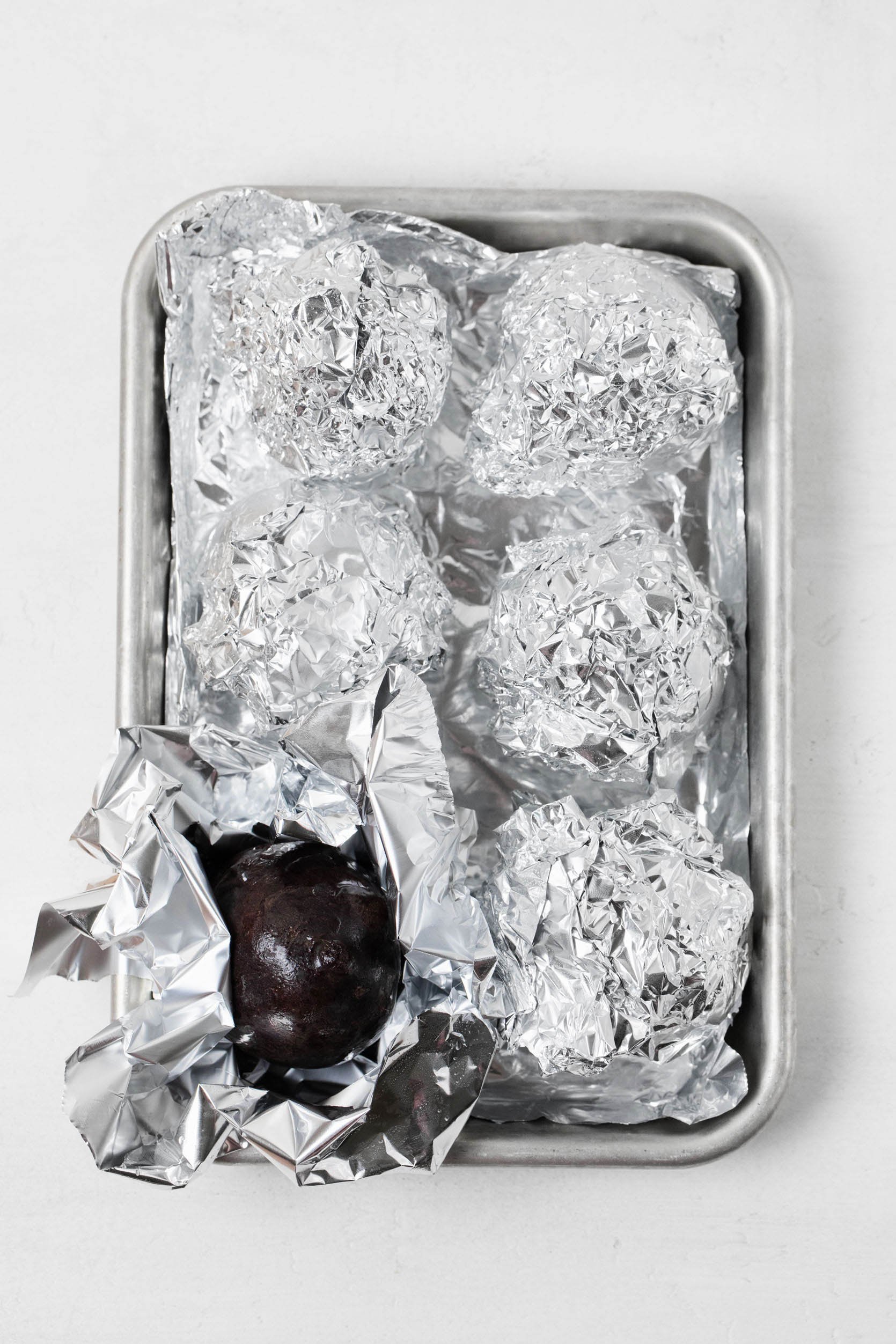 A small, aluminum baking tray holds foil-wrapped vegetables.