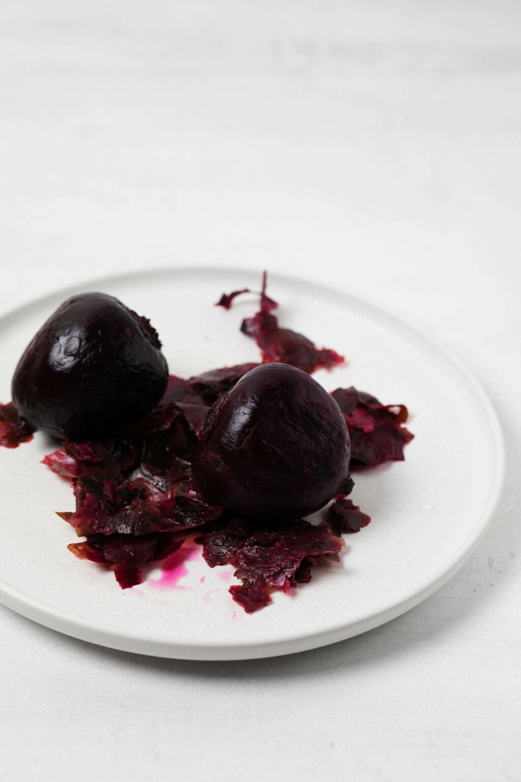 Roasted beets have just had their skins peeled off. The peeled beets rest on a white plate.