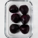 Red, roasted beets have been meal prepped are are held in a clear, glass storage container.