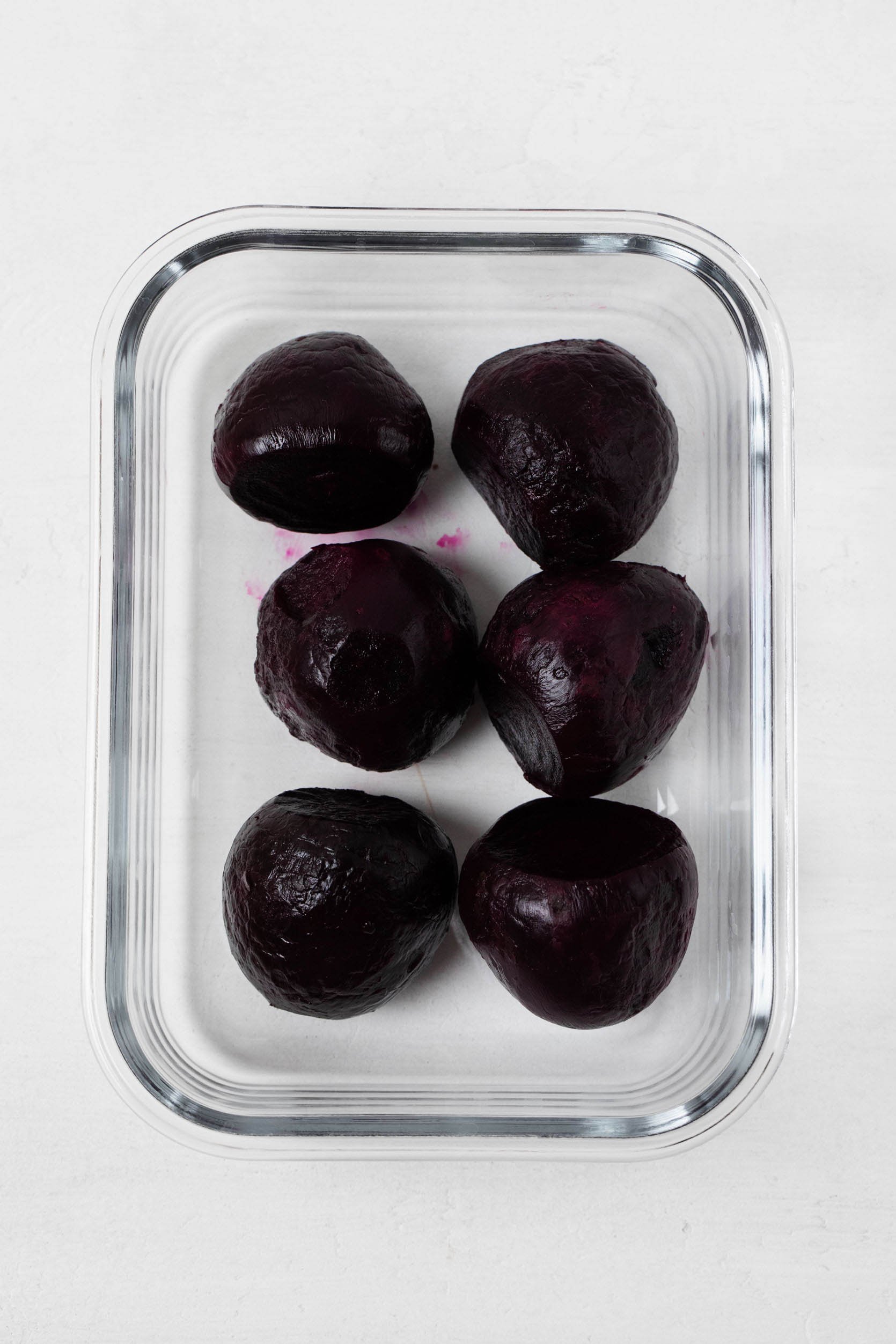 Red, roasted beets have been meal prepped are are held in a clear, glass storage container.