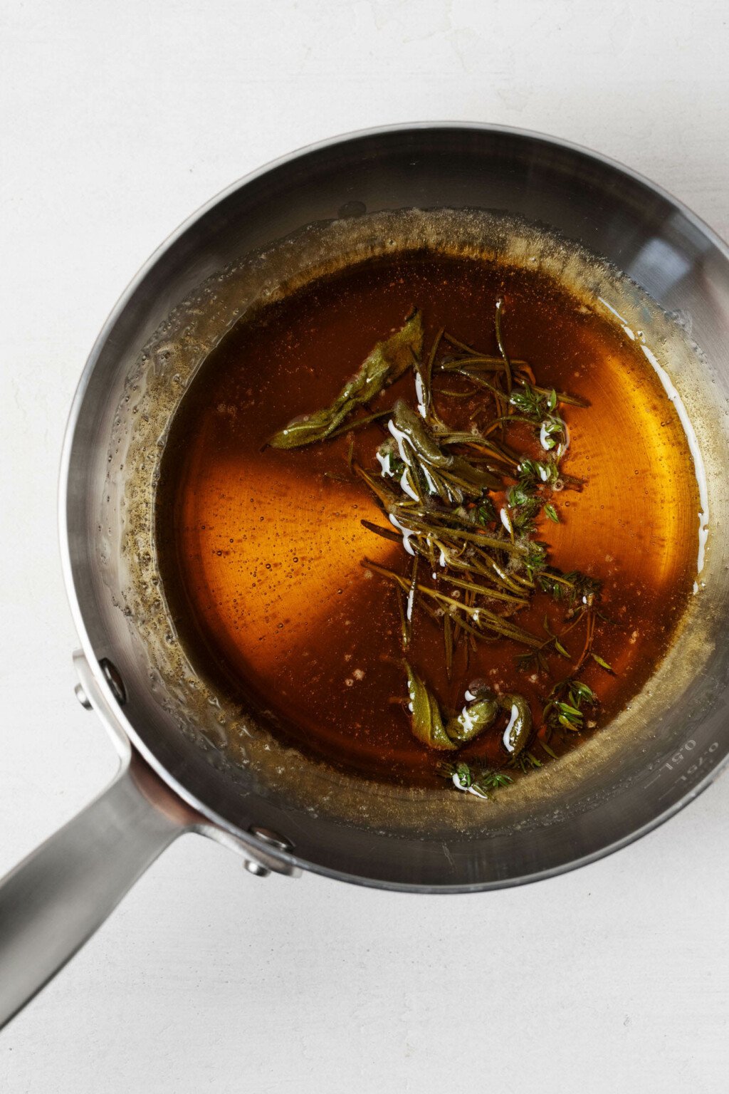 A small, metal saucepan holds warm syrup that's been infused with herbs.