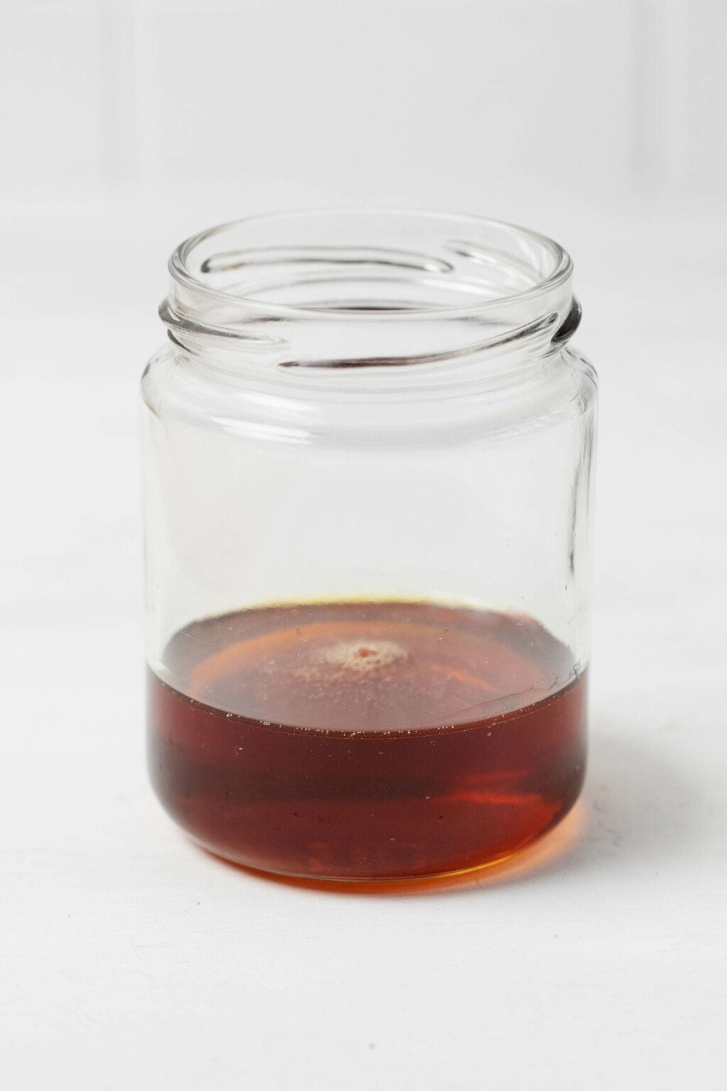 A jar of herb infused agave syrup rests on a white surface.