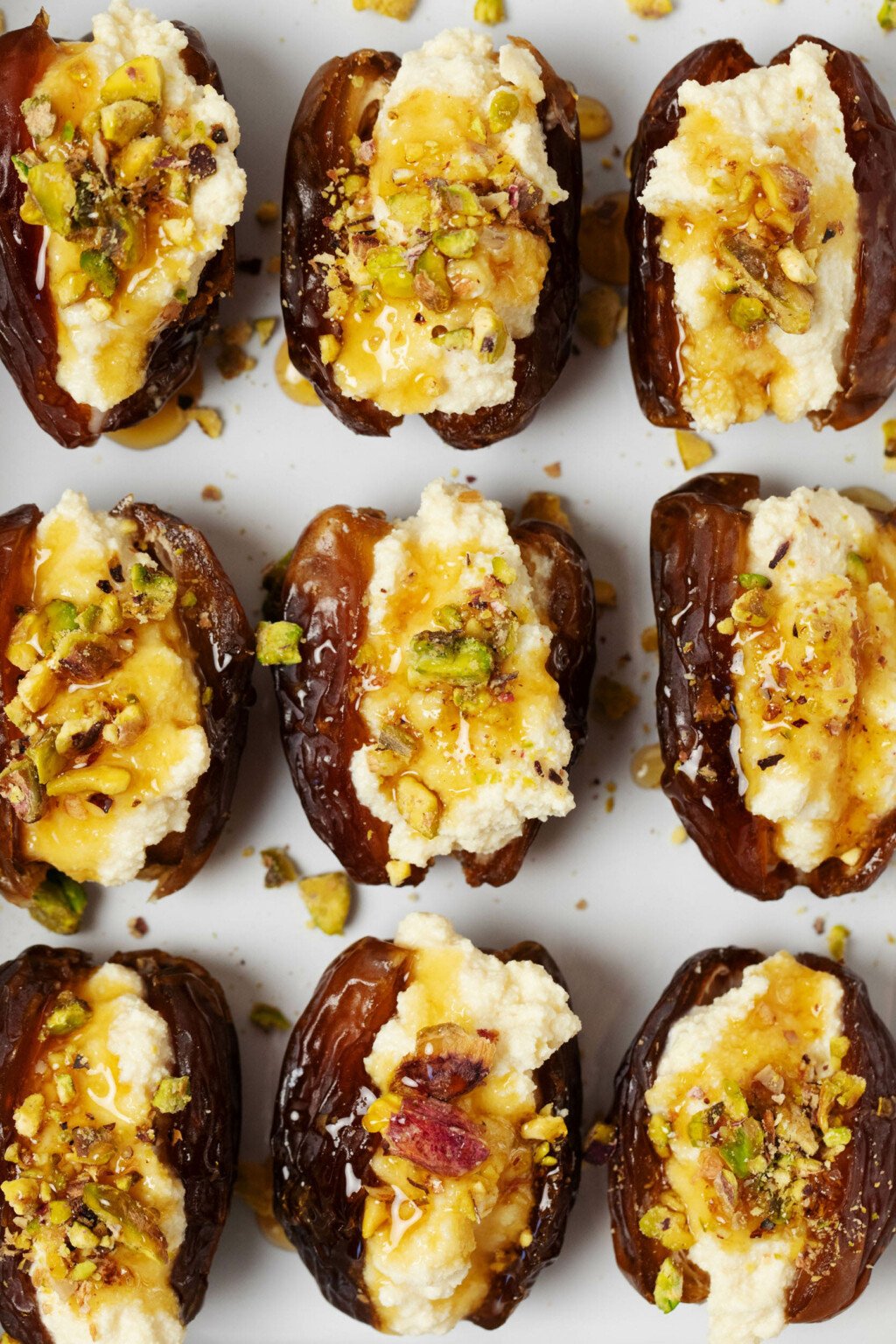 A close-up, overhead image of stuffed dates, which have been made with vegan cashew cheese. The dates are topped with chopped pistachio nuts and drizzled with herb infused syrup.