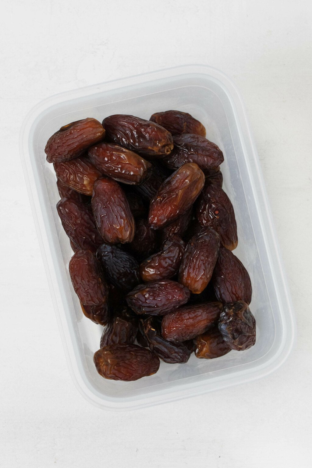 A storage container has been filled with brown, pitted Medjool dates.