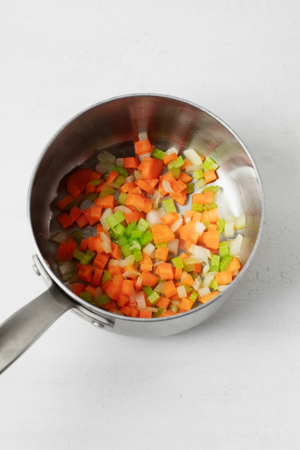A mirepoix mix has been put into a metal saucepan, which rests on a white surface.