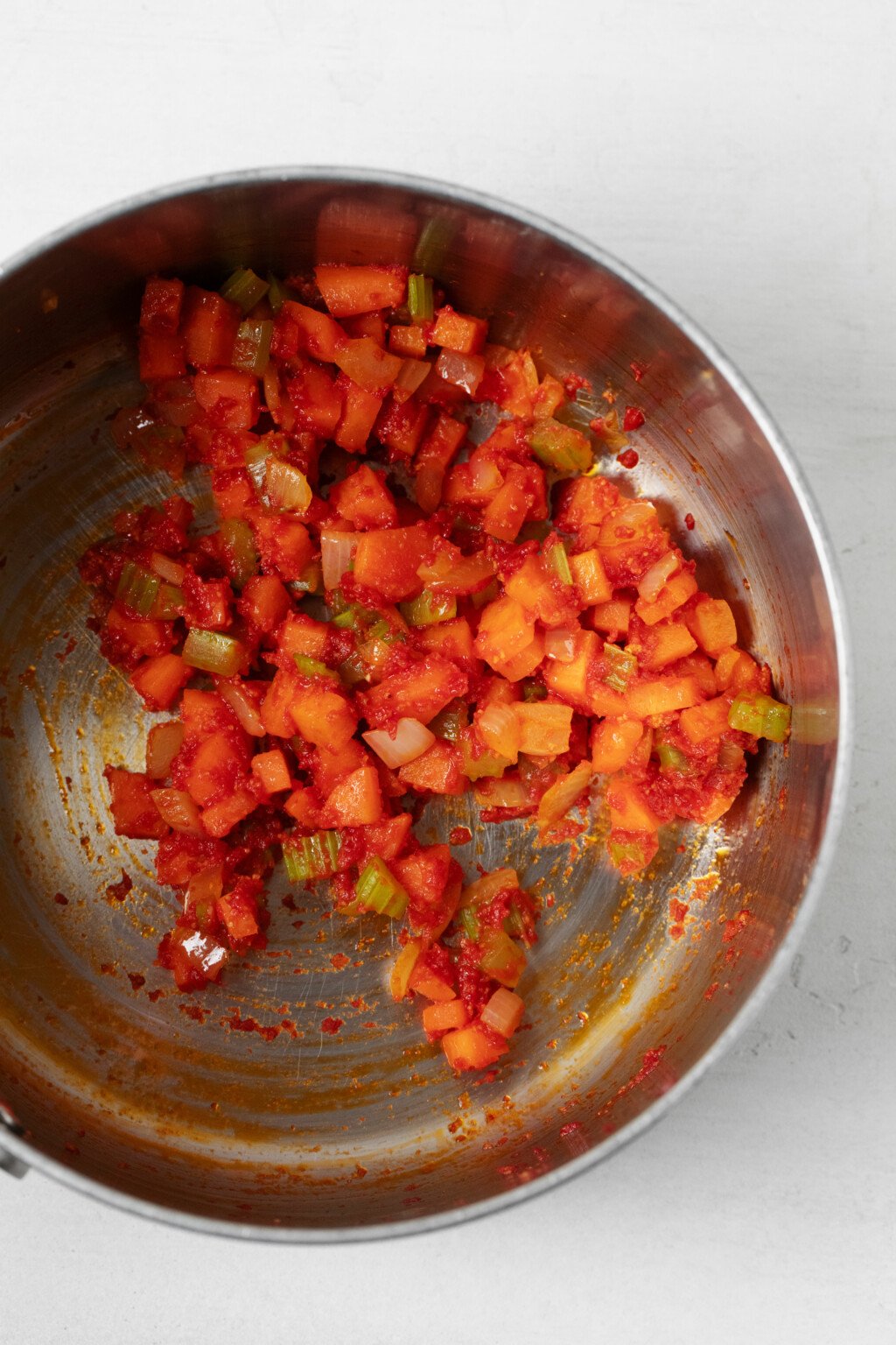 Vegetables and tomato paste are being sautéed in a metal sauce pan.