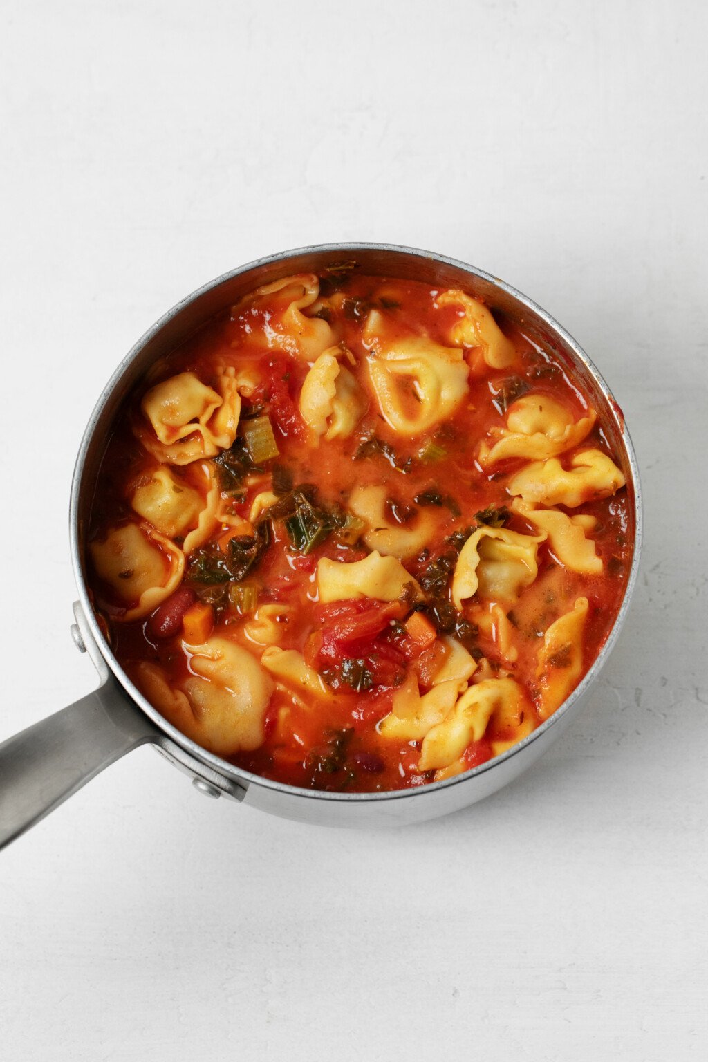 A saucepan holds tomatoes, beans, and vegan stuffed pasta.