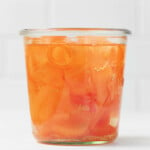 An angled photograph of a Weck mason jar, which is holding orange, pickled carrot ribbons.