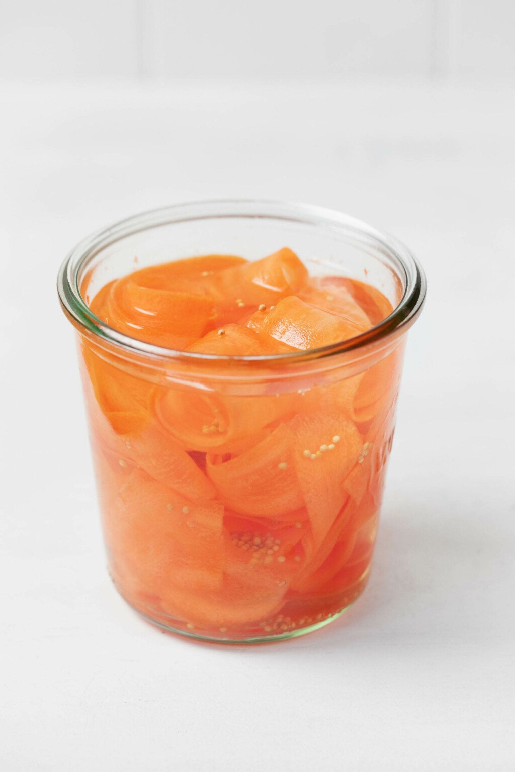A clear, glass mason jar holds shaved carrots that have been submerged in pickling juice.