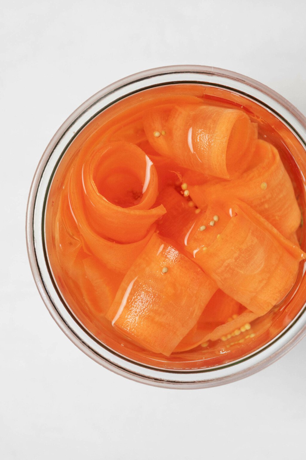 Μια εικόνα από πάνω από ένα βάζο γεμάτο με κορδέλες καρότου τουρσί.