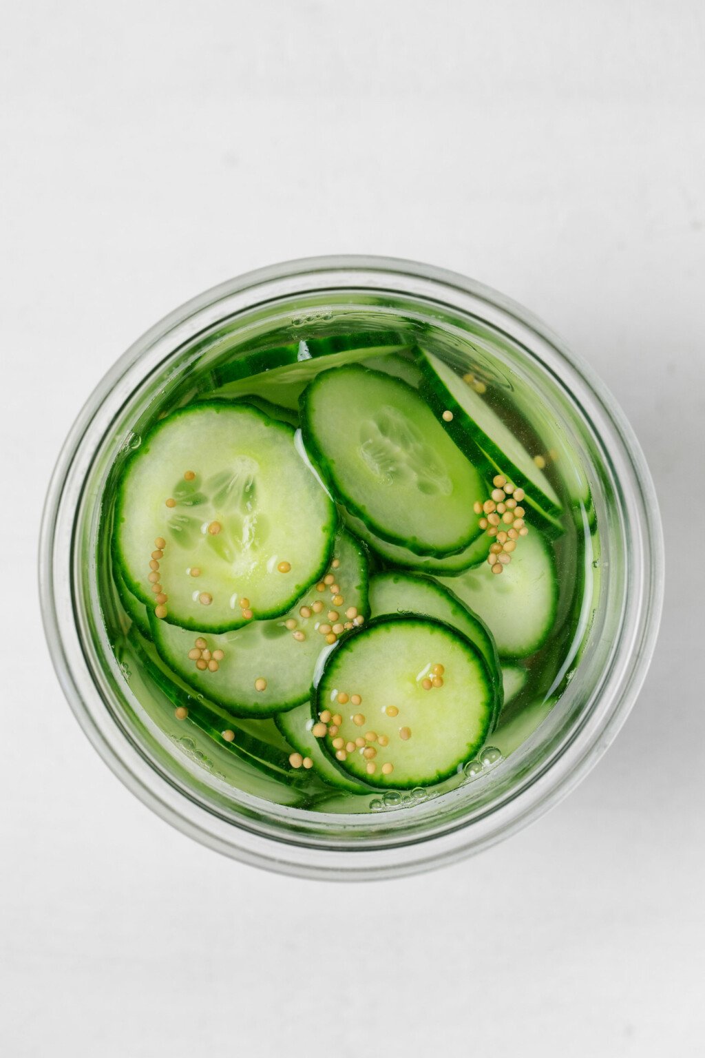 An overhead image of thinly sliced, pickled cucumbers and mustard seeds.