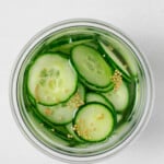 An overhead image of thinly sliced, pickled cucumbers and mustard seeds.