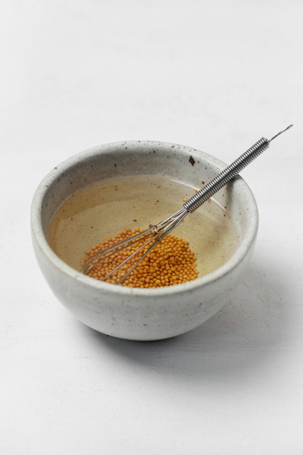 A small pinch bowl is filled with water, vinegar, and mustard seeds.