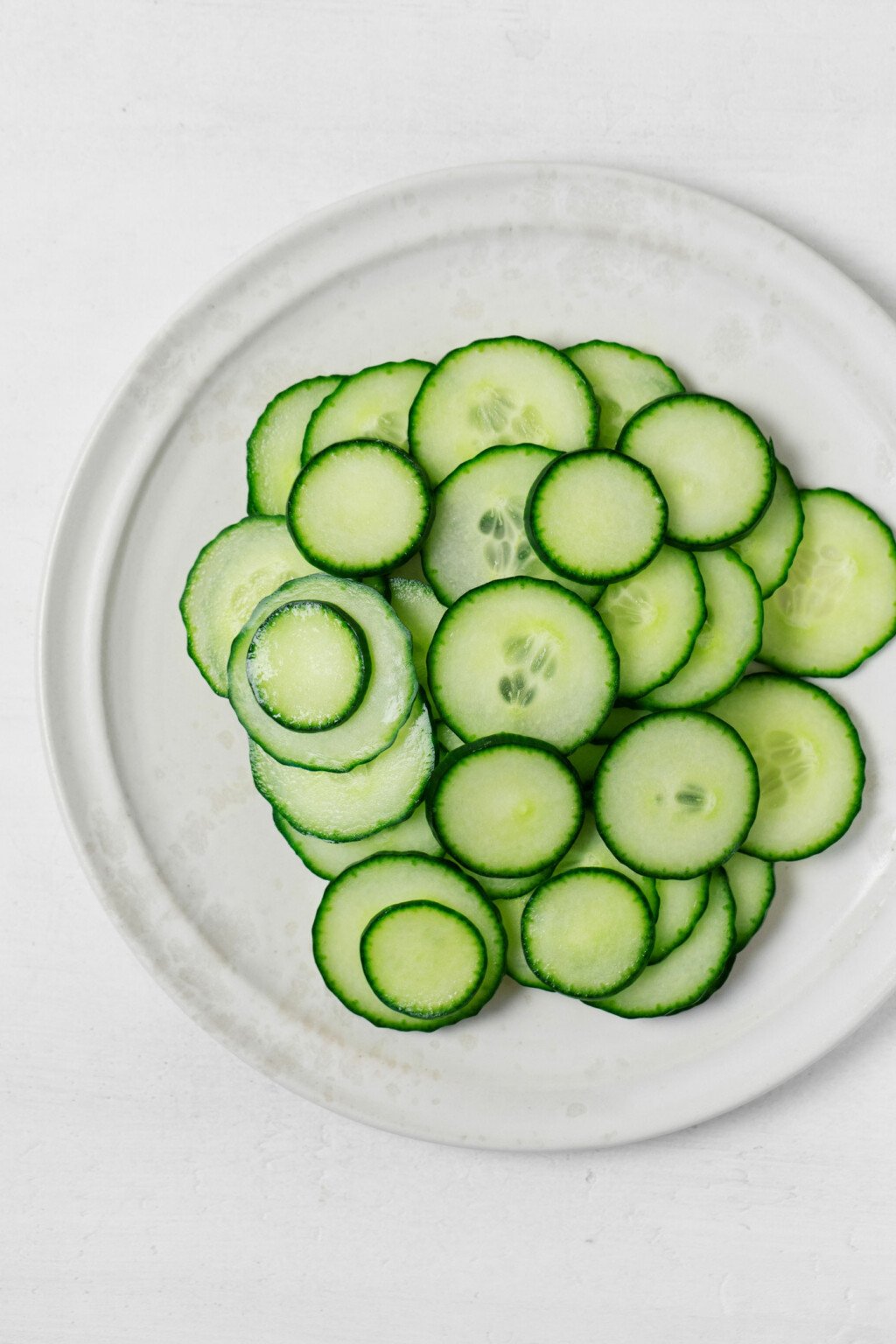 Crosswise sliced cucumbers are resting on a white plate.