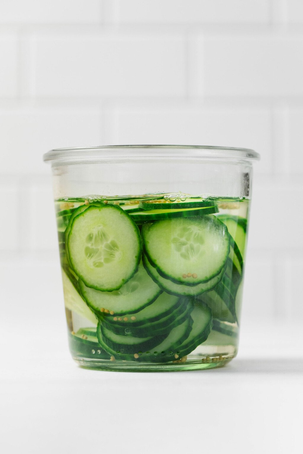 A glass mason jar has been filled with crisp, bright green sliced vegetables and pickling liquid.