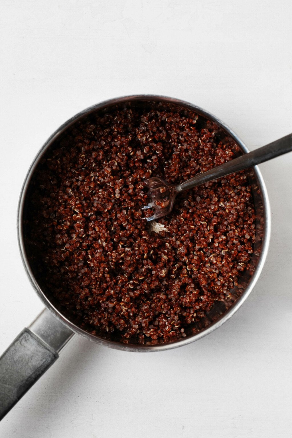 A stainless steel saucepan is filled with fluffy, freshly cooked red quinoa.