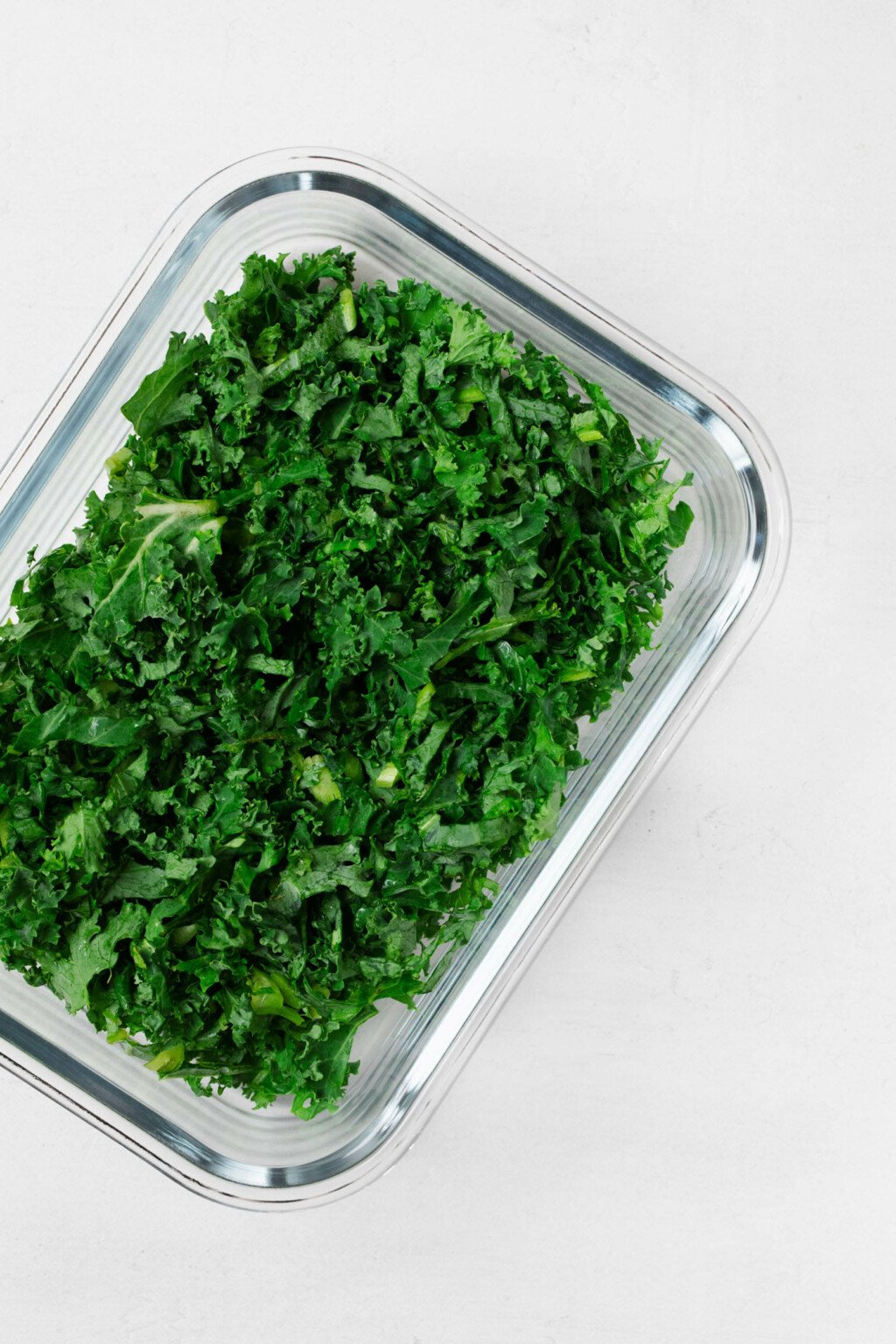 A glass storage container holds bright green pieces of chopped kale.