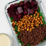 A glass, rectangular storage container holds the components for a plant-based meal, with a small container of dressing nearby.