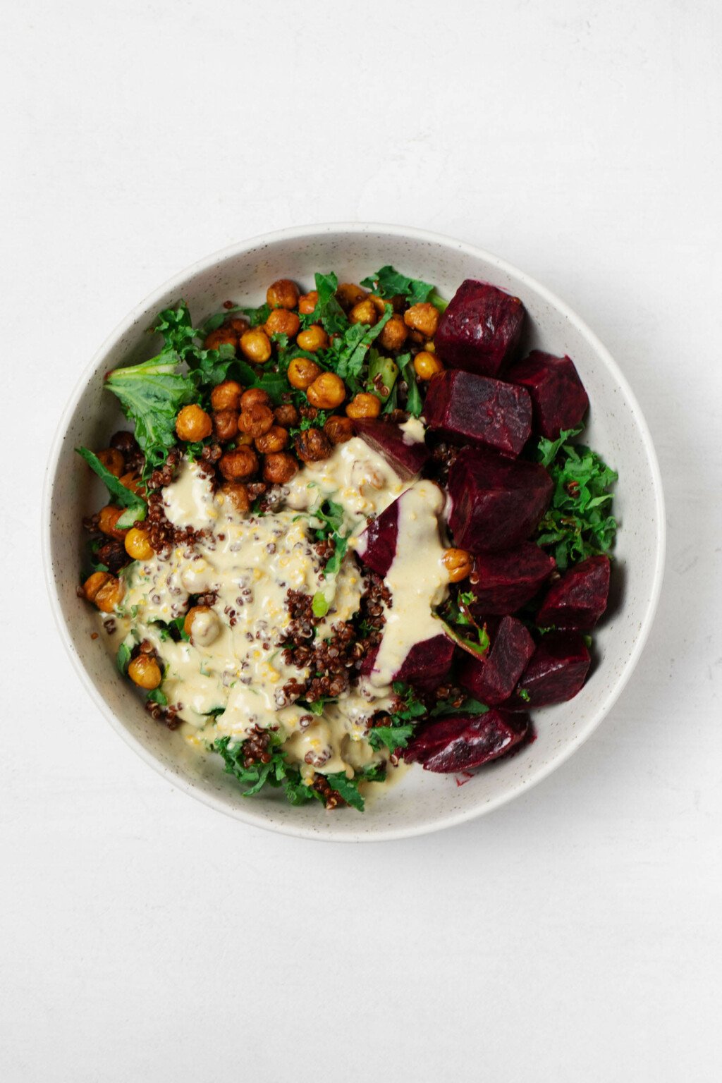 A round, white ceramic bowl holds cooked quinoa, chickpeas, beets, and finely chopped kale.